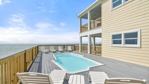 A deck with a pool, white chairs, and a view of the ocean. - Shamrock Shores - Gulf Front West End Pet Friendly Property With Room For Everyone. 3 Master Suites! 6 Bedroom Home by RedAwning (Dauphin Island)