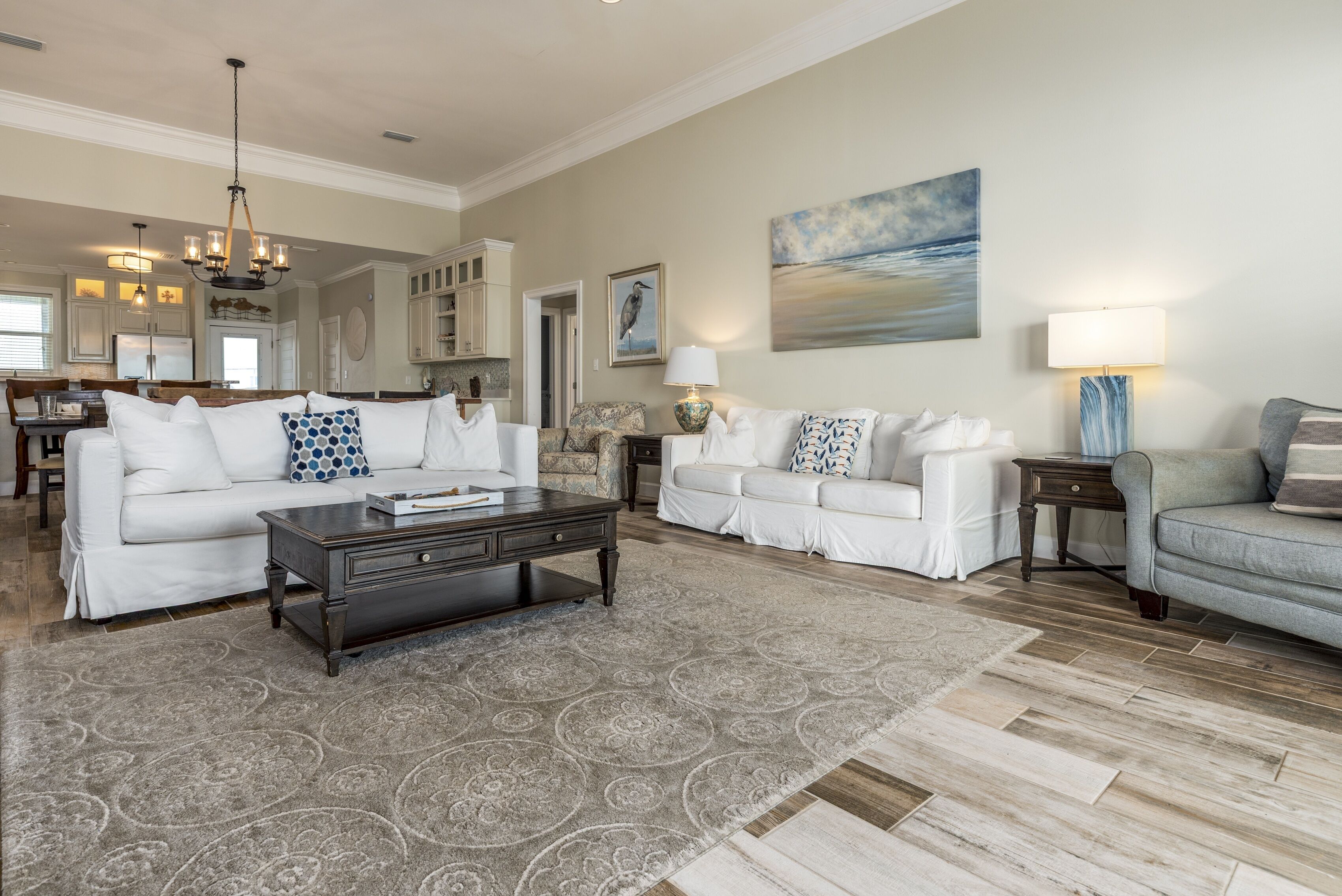 A spacious living room with a large coffee table, two white sofas, a patterned rug, and a view of the kitchen and dining area.
