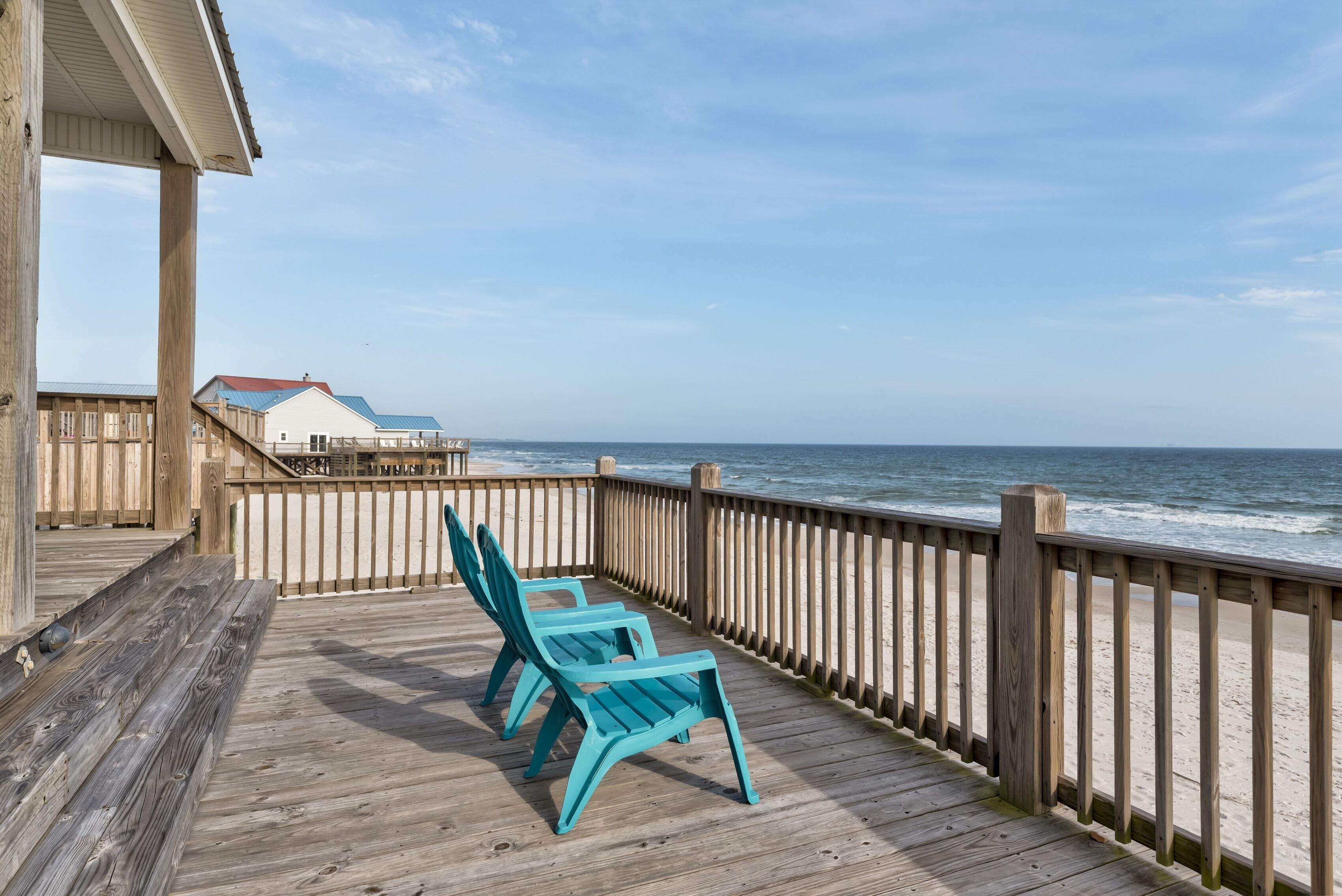 A wooden deck with two chairs overlooking the ocean.