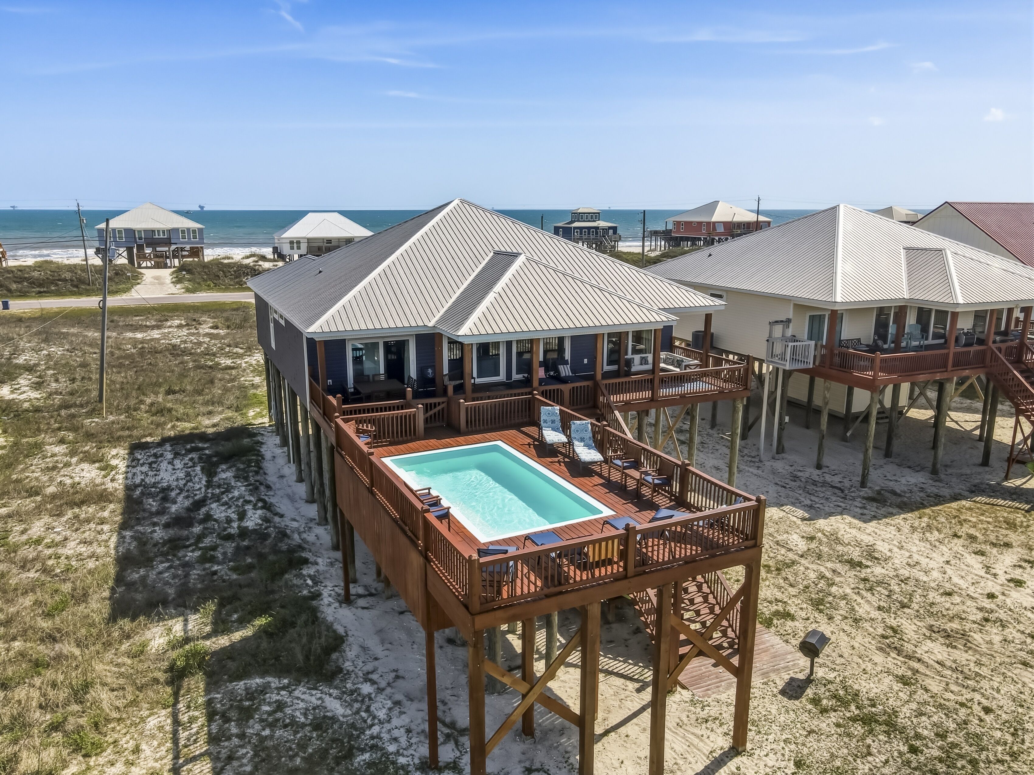 A beachfront property with a pool, wooden deck, and multiple rooms with views of the ocean.