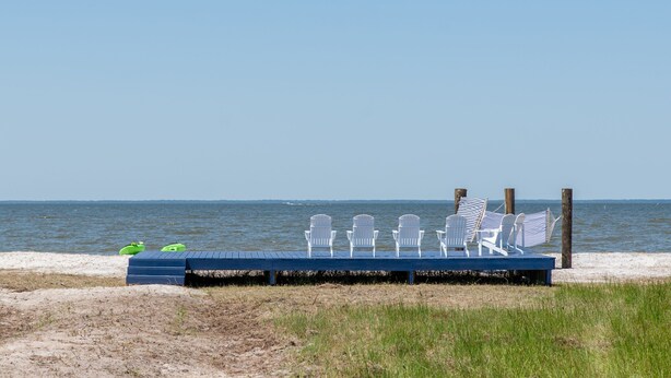 Ein Sitzbereich am Strand mit weißen Stühlen und einer blauen Plattform mit Blick auf den Ozean.