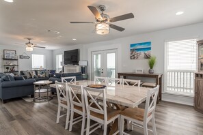 A spacious living room with a large sofa, a dining table with chairs, a ceiling fan, and a TV.
