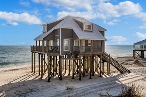 A beach house with a wooden deck and a staircase leading to the main floor.