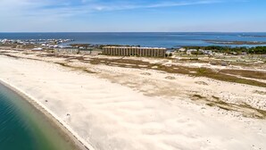 An aerial view of a coastal area with a large sandy beach, a marina, and a hotel with multiple floors and a flat roof. - Calm Seas - Holiday Isle #119 - Tremendous Views, A Beautiful Gulf Front Pool, A Heated Indoor Pool, Jacuzzi, Steam Room, And Gulf View Fitness Center. 2 Bedroom Condo by RedAwning (Dauphin Island)