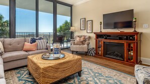 A living room with a sofa, armchair, and coffee table, a fireplace, and a TV. - Calm Seas - Holiday Isle #119 - Tremendous Views, A Beautiful Gulf Front Pool, A Heated Indoor Pool, Jacuzzi, Steam Room, And Gulf View Fitness Center. 2 Bedroom Condo by RedAwning (Dauphin Island)