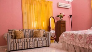 Un dormitorio con un sofá estampado, una cama con colcha floral, un aparador, un espejo y una cortina amarilla.