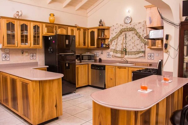A kitchen with wooden cabinets, a black refrigerator, a microwave, and a dishwasher. There are two small glasses on the counter.