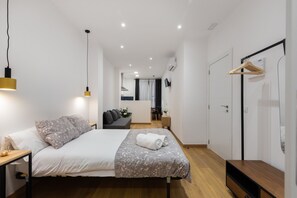 Une chambre d’hôtel moderne avec un lit bien fait, une table de chevet en bois, une lampe de chevet, une armoire et un miroir au mur.