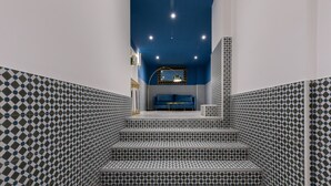 Un escalier recouvert de carreaux décorés mène à une pièce dont un mur est bleu et qui contient un miroir.