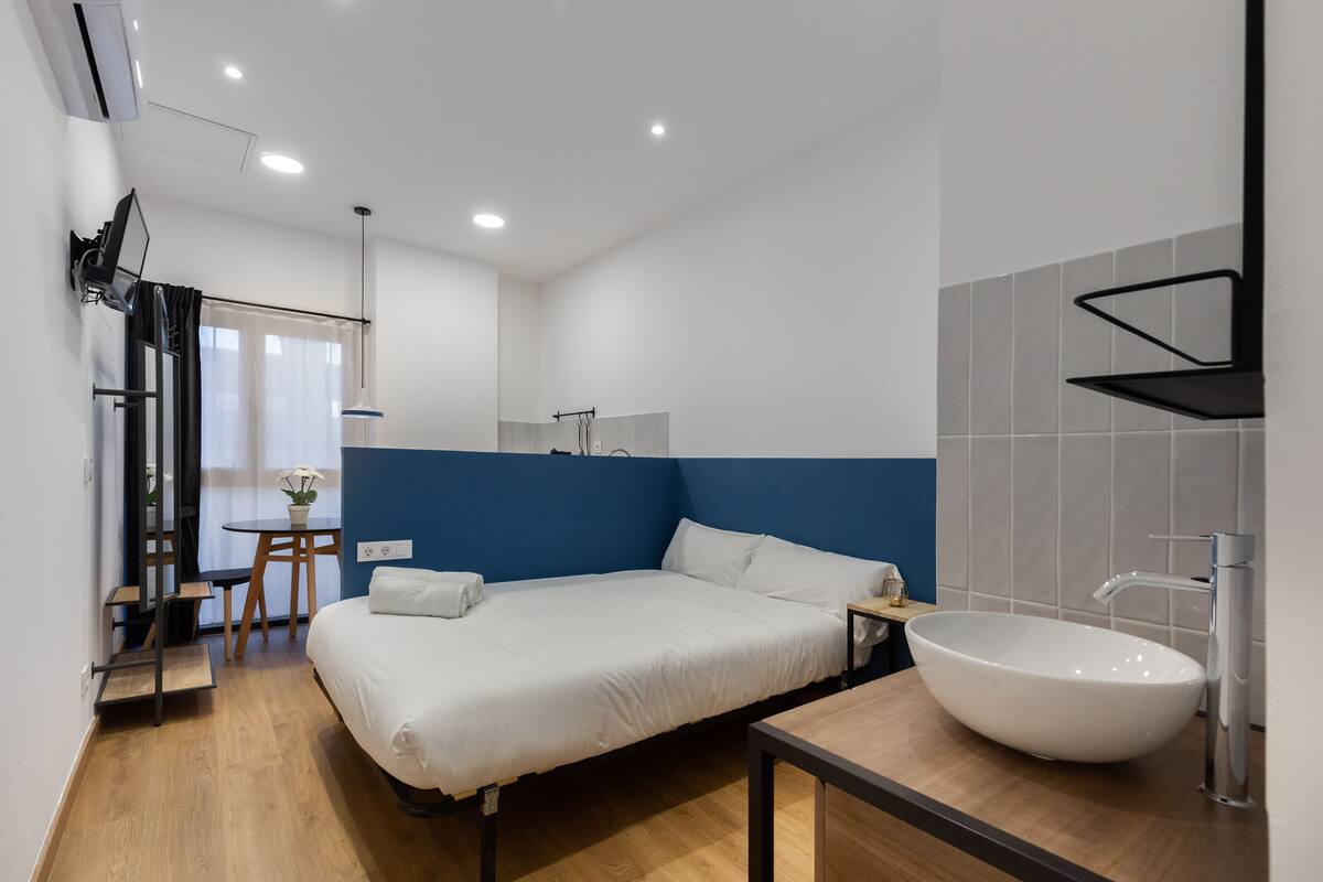 A modern hotel room with a large bed, a round white sink, and a small table with a chair.