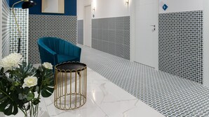Une salle de bain moderne avec un mur d’accent bleu, une chaise turquoise, un vase doré et un sol à motifs.