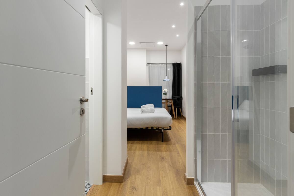 A modern hotel room with a bed, a desk, and a shower area.