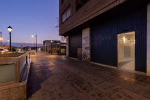 Une rue urbaine de nuit, avec un bâtiment en briques, un magasin fermé et un trottoir carrelé.