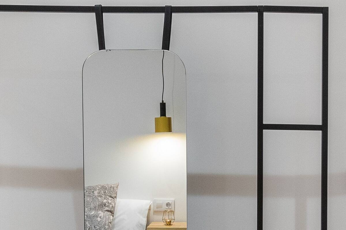 A bedroom with a wooden dresser, a mirror, and a bedside table with a lamp.