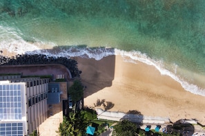 An aerial view of a beach with a sandy shore, a rocky breakwater, and a building with solar panels.
