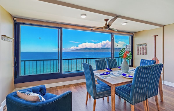 A dining area with a view of the ocean, a ceiling fan, and a dining table set for four.