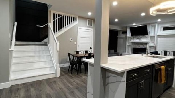 A modern kitchen with a central island, dark wood flooring, and a staircase leading to another level. - Minutes from Anything Downtown Indy! (Indianapolis)
