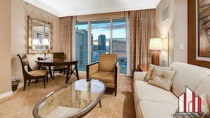 A hotel room with a dining table, two chairs, a sofa, a glass coffee table, and a large window offering a city view. - MGM Signature-  Studio F1 Track Strip View Balcony (Las Vegas)