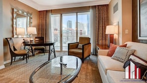 A hotel room with a dining table, two chairs, a sofa, a glass coffee table, and a large window offering a city view. - Luxury Studio | Jacuzzi, Balcony & Full Bath (Las Vegas)