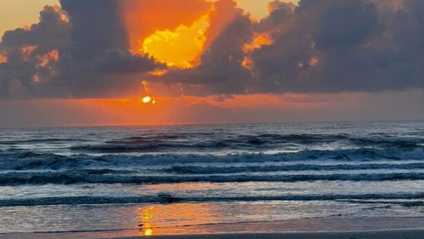 Un atardecer sobre el océano con nubes reflejándose en el agua.