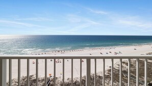 Strandudsigt fra en balkon med gelænder, sandstrand og hav.