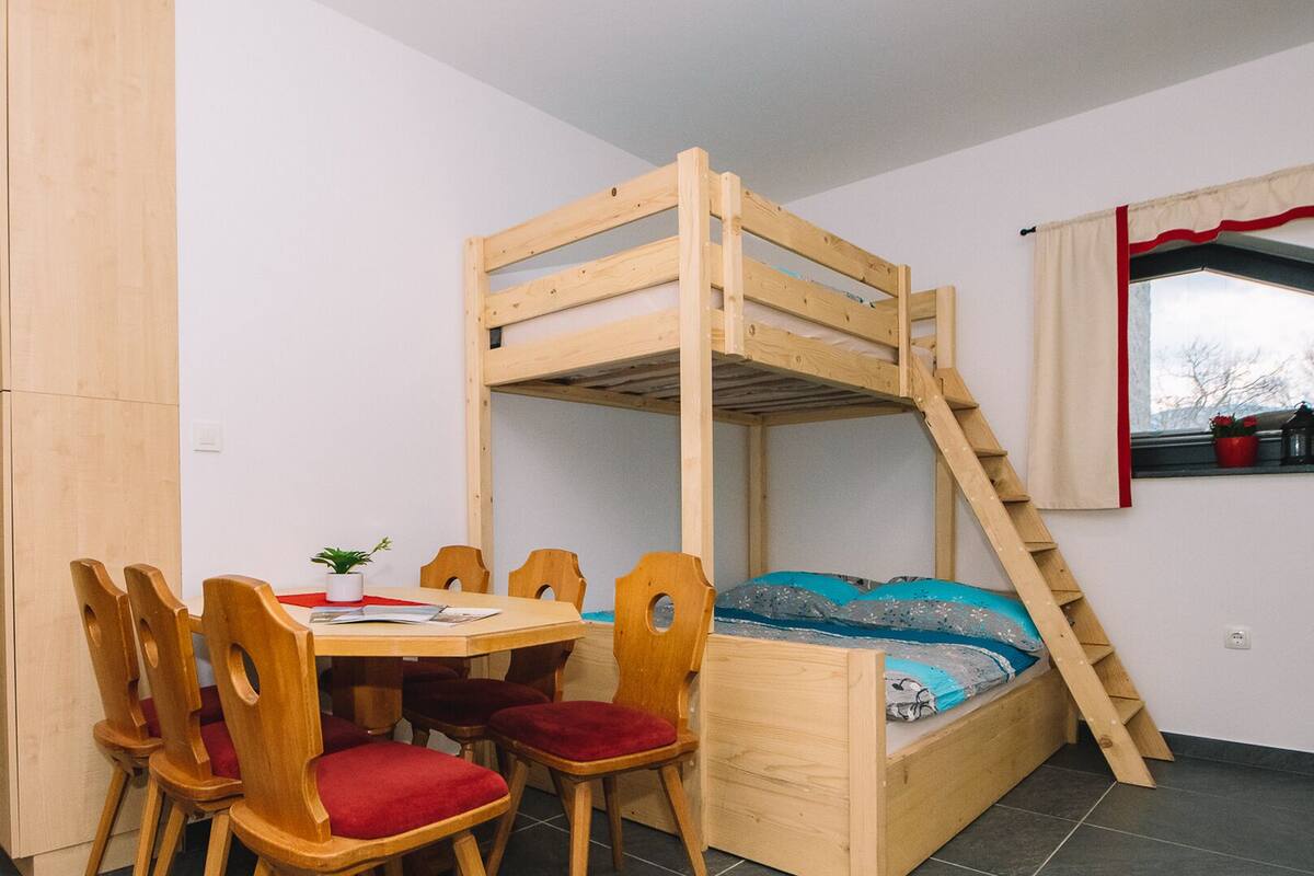 Ein Zimmer mit einem Etagenbett, Holzstühlen, einem Tisch und einem Fenster mit Vorhängen.