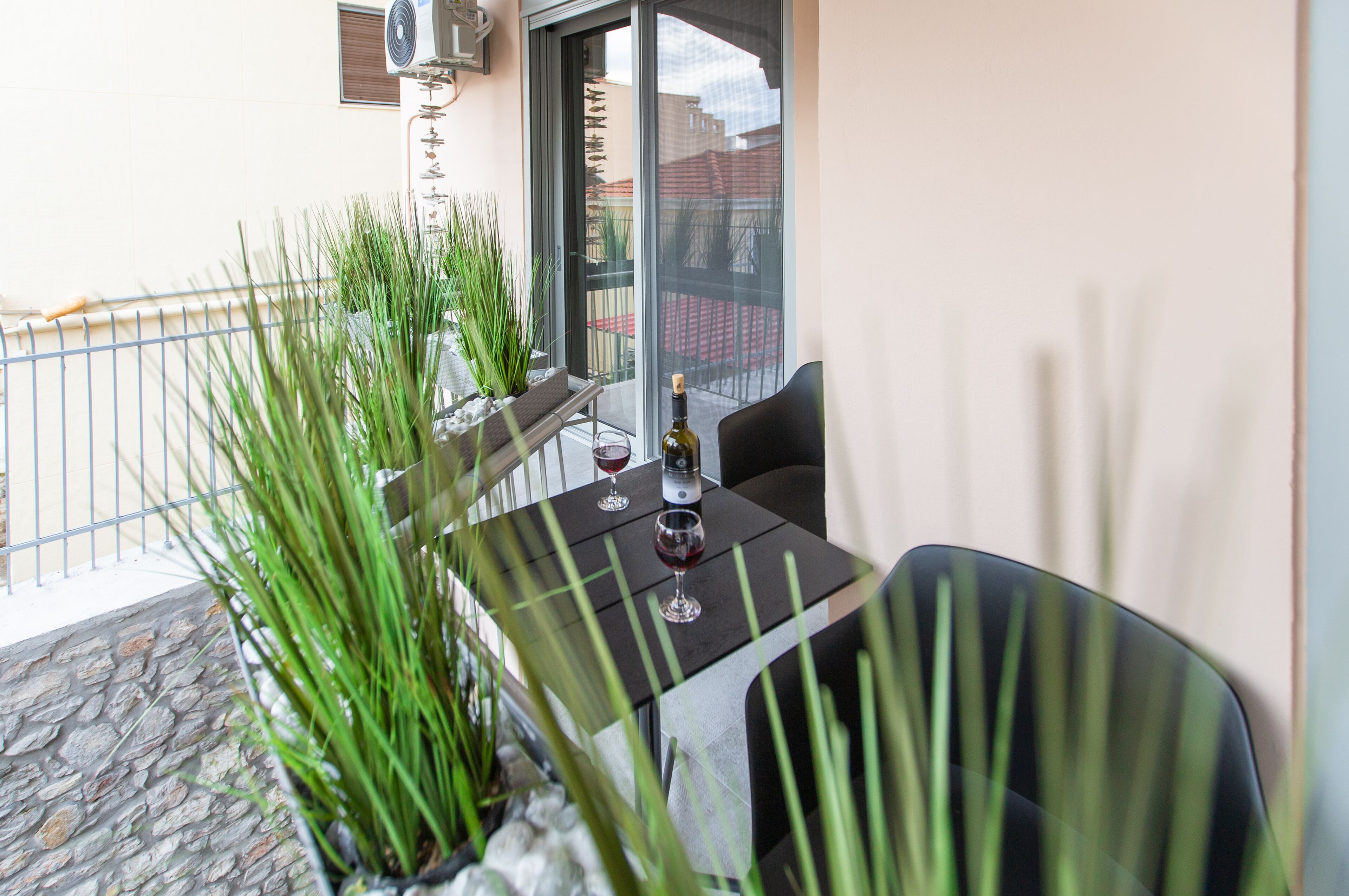 En balkon med et bord, stole, plantekasser og en flaske vin.