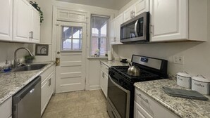 A compact kitchen with white cabinets, a stainless steel dishwasher, a microwave, a stove, and a sink. There are two containers labeled 'Tea' and 'Coffee'. - 6649 1E | Garden Style Studio Near Forest Park (St. Louis)