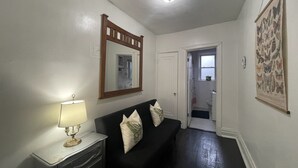 A hallway with a black sofa, a mirror, a lamp, and a butterfly wall hanging. - 6649 1E | Garden Style Studio Near Forest Park (St. Louis)