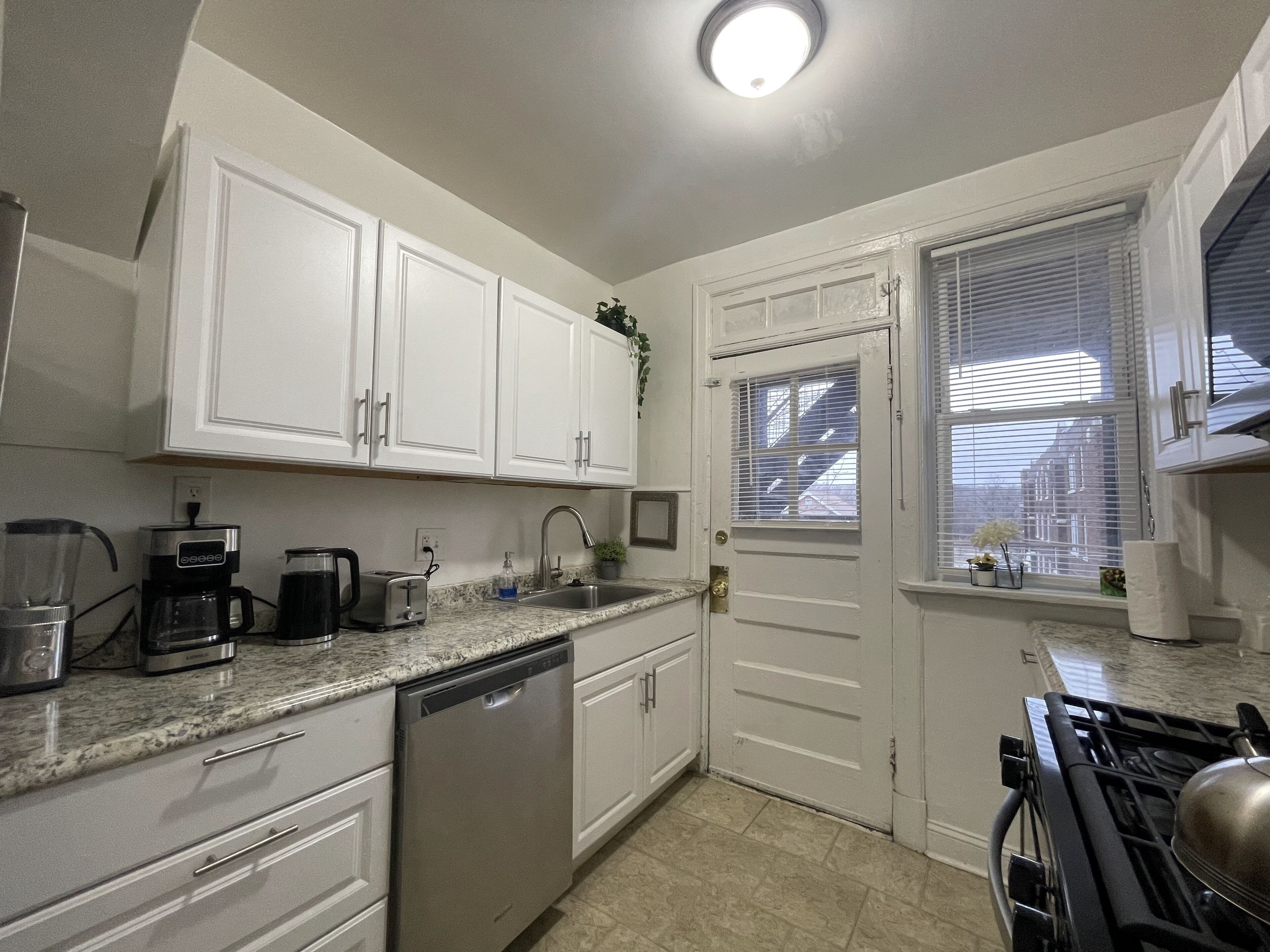 A compact kitchen with white cabinets, a dishwasher, a coffee maker, a sink, and a stove.
