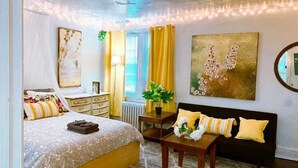 A bedroom with a bed, bedside table, lamp, and a large painting. - 6649 1E | Garden Style Studio Near Forest Park (St. Louis)