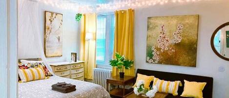 A bedroom with a bed, bedside table, lamp, and a large painting.
