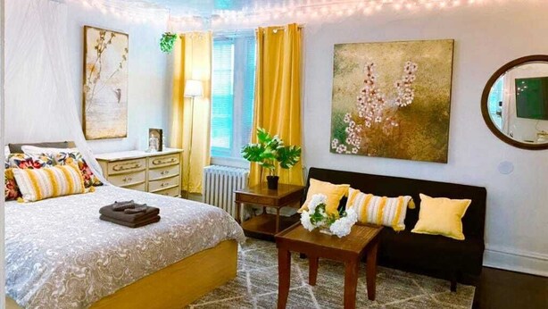 A bedroom with a bed, bedside table, and a large painting on the wall. - 6649 1E | Garden Style Studio Near Forest Park (St. Louis)