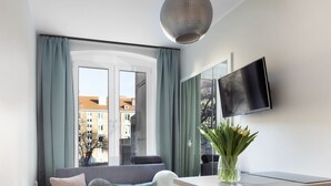 A modern living room with a sofa, a desk, a chair, a TV, and a window with curtains. - Elite Apartments Garncarska (Gdansk)