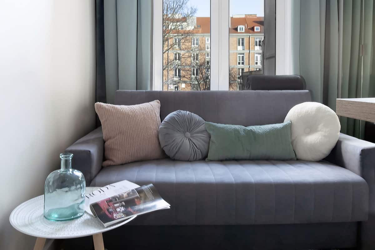 A modern living room with a grey sofa, a glass vase, and a magazine on a small round table.