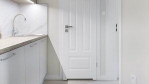 A narrow hallway with a kitchen area on the left, featuring a sink and cabinets. A white door is at the end of the hallway. - Elite Apartments Garncarska (Gdansk)
