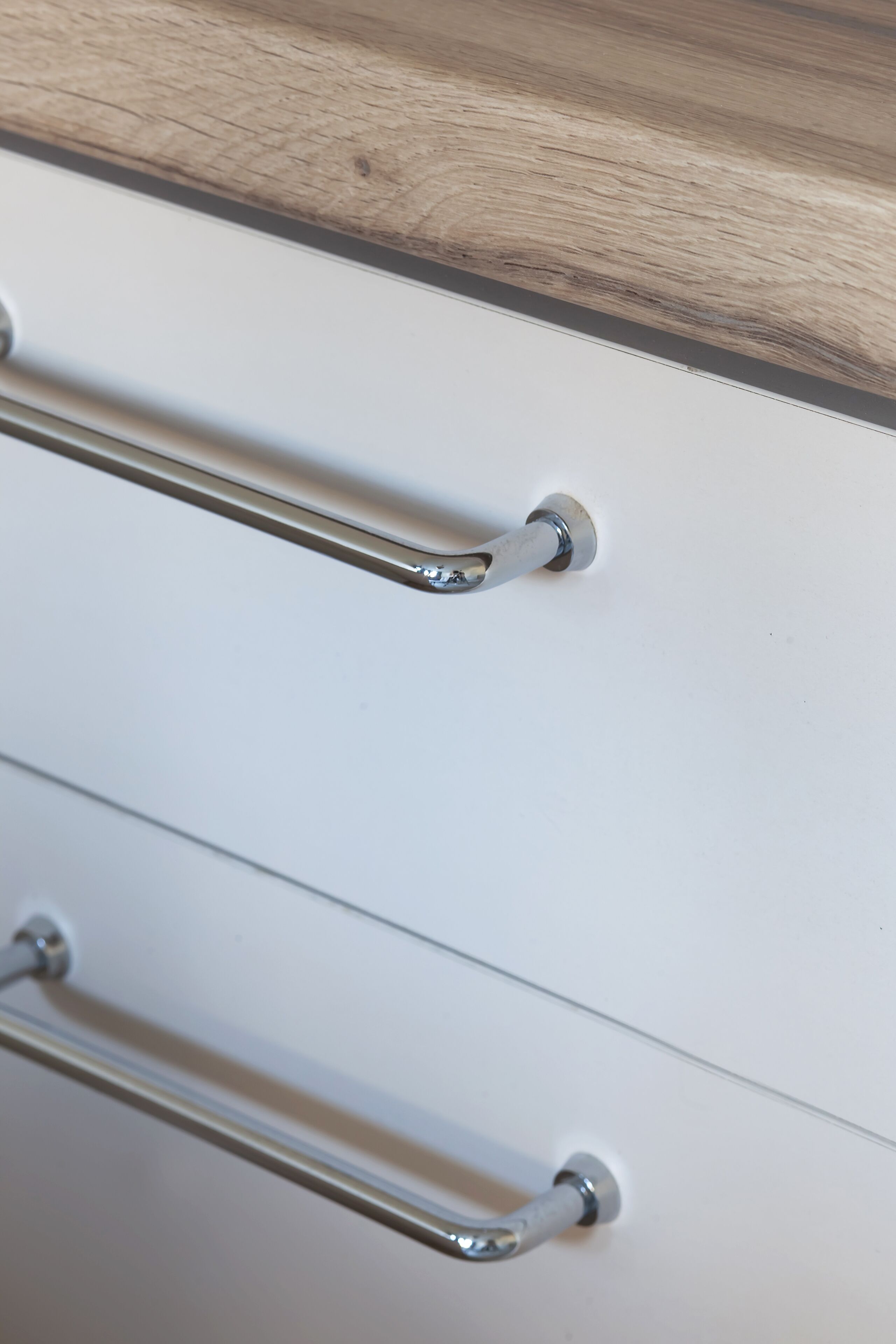 A close-up of a drawer with metallic handles and a wooden surface above.