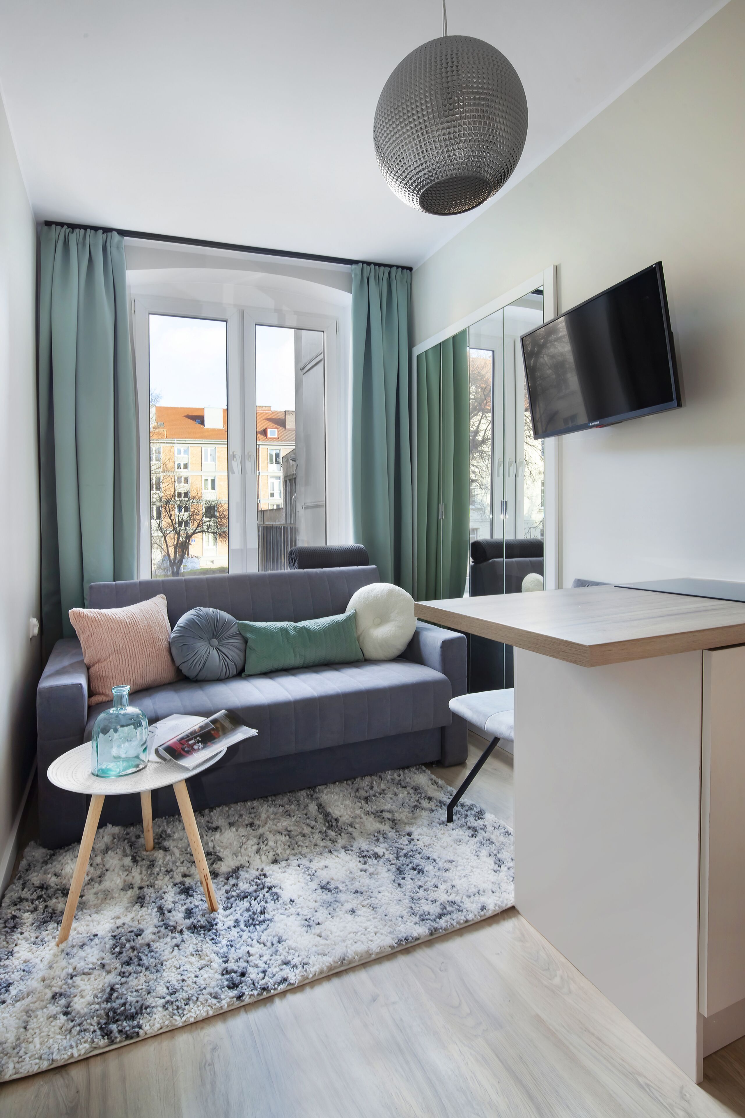 A modern living room with a grey sofa, a small round table, and a TV mounted on the wall.
