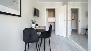 A modern dining area with a table, chairs, a potted plant, and a mounted TV. - Elite Apartments Garncarska (Gdansk)