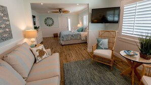 A cozy bedroom with a bed, a chair, a TV, and a window with blinds.