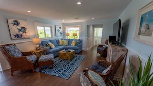 A living room with a blue sofa, wicker chairs, a coffee table, and artwork on the walls.