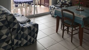 Un saló amb un sofà, una taula de dinar amb cadires, una televisió i una porta corredissa de vidre que dona a una zona exterior amb una taula i cadires.