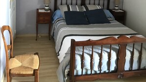 Un dormitori amb llit, taules de nit, una cadira i un quadre penjat a la paret.