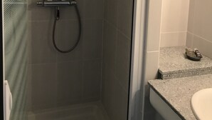 Zona de bany amb porta de vidre, plat de dutxa i mànega de dutxa.