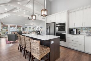 A modern kitchen with white cabinets, a central island with bar stools, stainless steel appliances, and pendant lighting. - Bella Rose: Saltwater Pool | Rec Room | Elevator (Corolla)