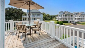 Une terrasse en bois avec une table et des chaises, un grand parasol et une vue sur une rangée de maisons.
