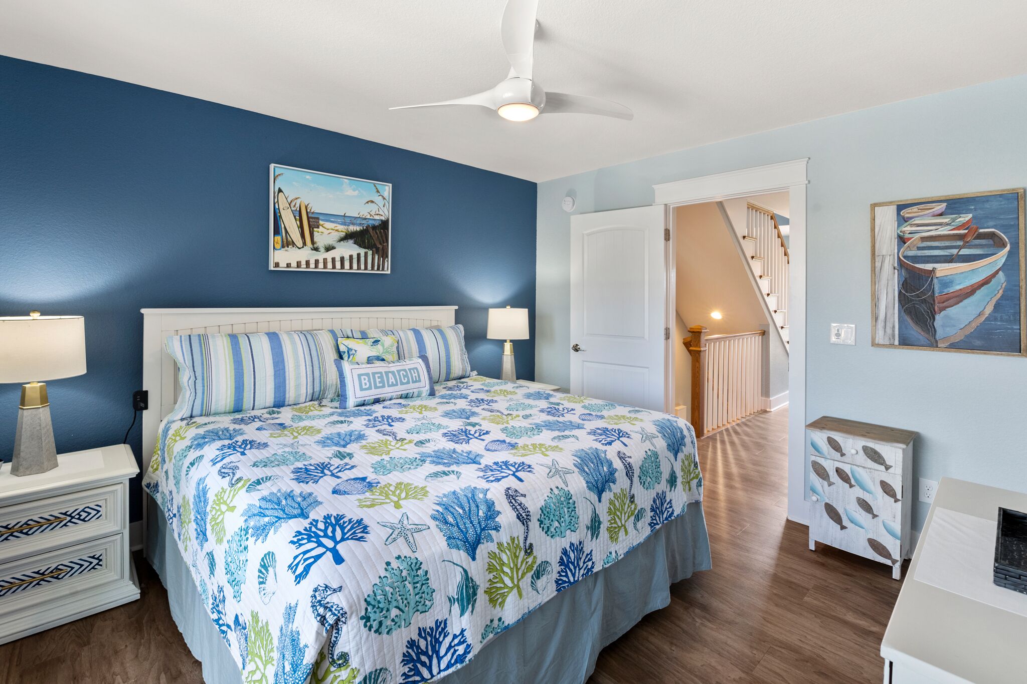 A bedroom with a bed, two bedside tables, a ceiling fan, and a door leading to a staircase.