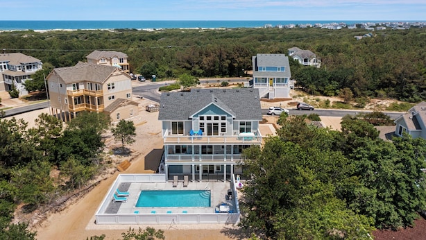 Une grande maison à deux étages avec une piscine, entourée d’arbres et offrant une vue sur la plage.