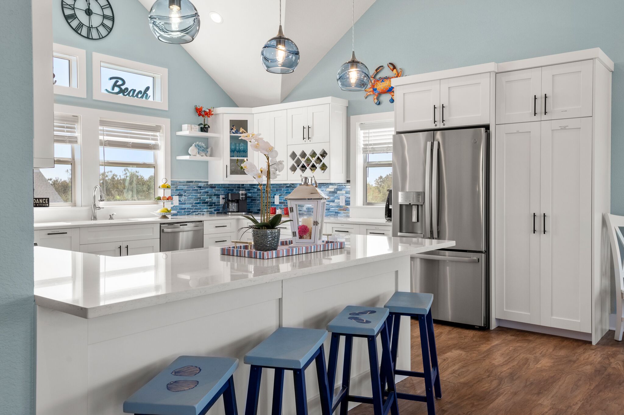 A modern kitchen with white cabinetry, a stainless steel refrigerator, and a large island with bar stools.