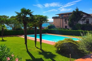 Une piscine entourée de pelouse bien entretenue, de palmiers et d’un bâtiment doté d’un toit en tuiles.